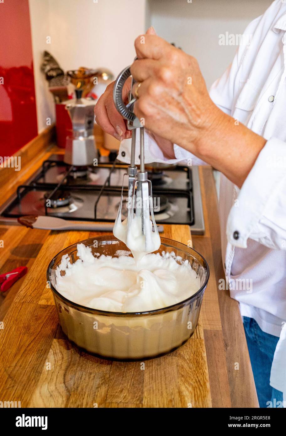 Woman home cook whisking up egg whites to stiff peaks by hand to make a
