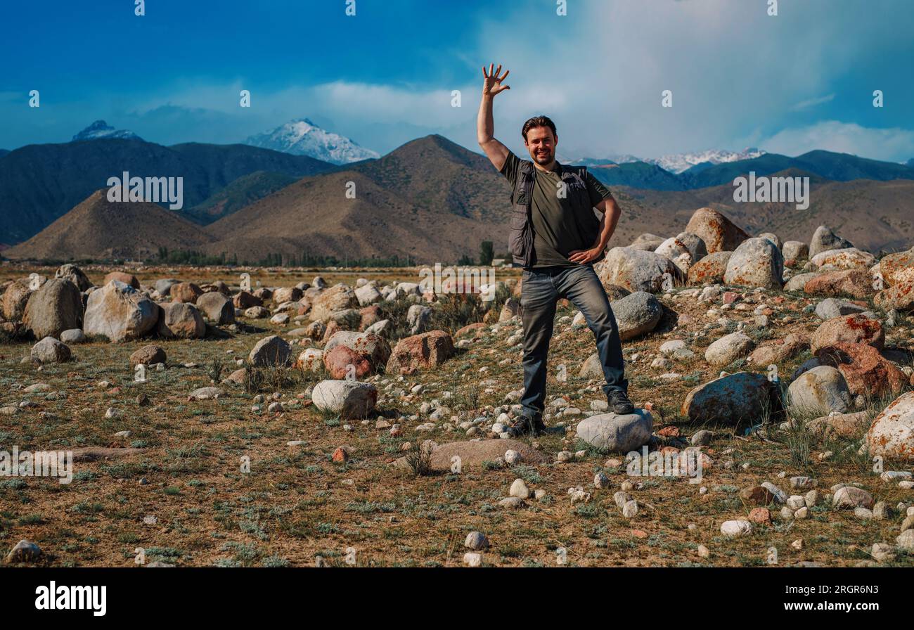 Young smiling man stands on mountain and waving his hand Stock Photo