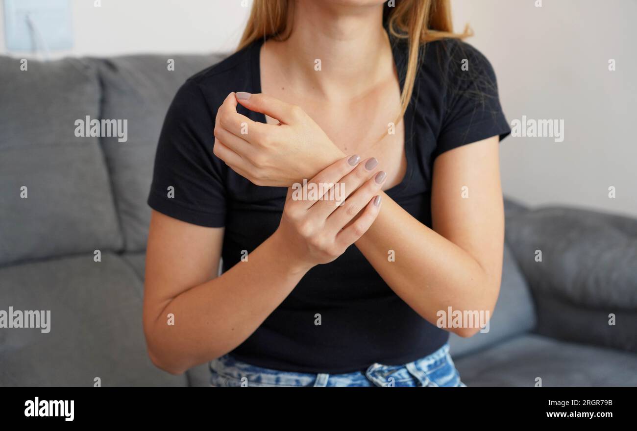 People, healthcare and problem concept. Unhappy young woman suffering from wrist pain sitting on sofa at home. Stock Photo