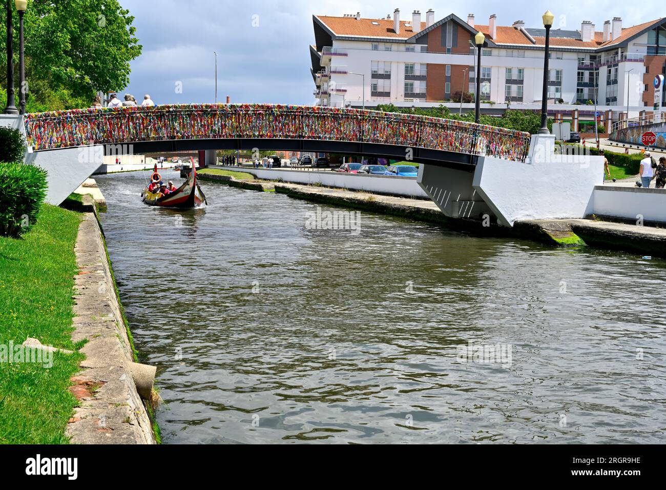 Bridge over canal covered in keepsake signed tags with traditional Moliceiro boat with tourists. Aveiro, Portugal Stock Photo