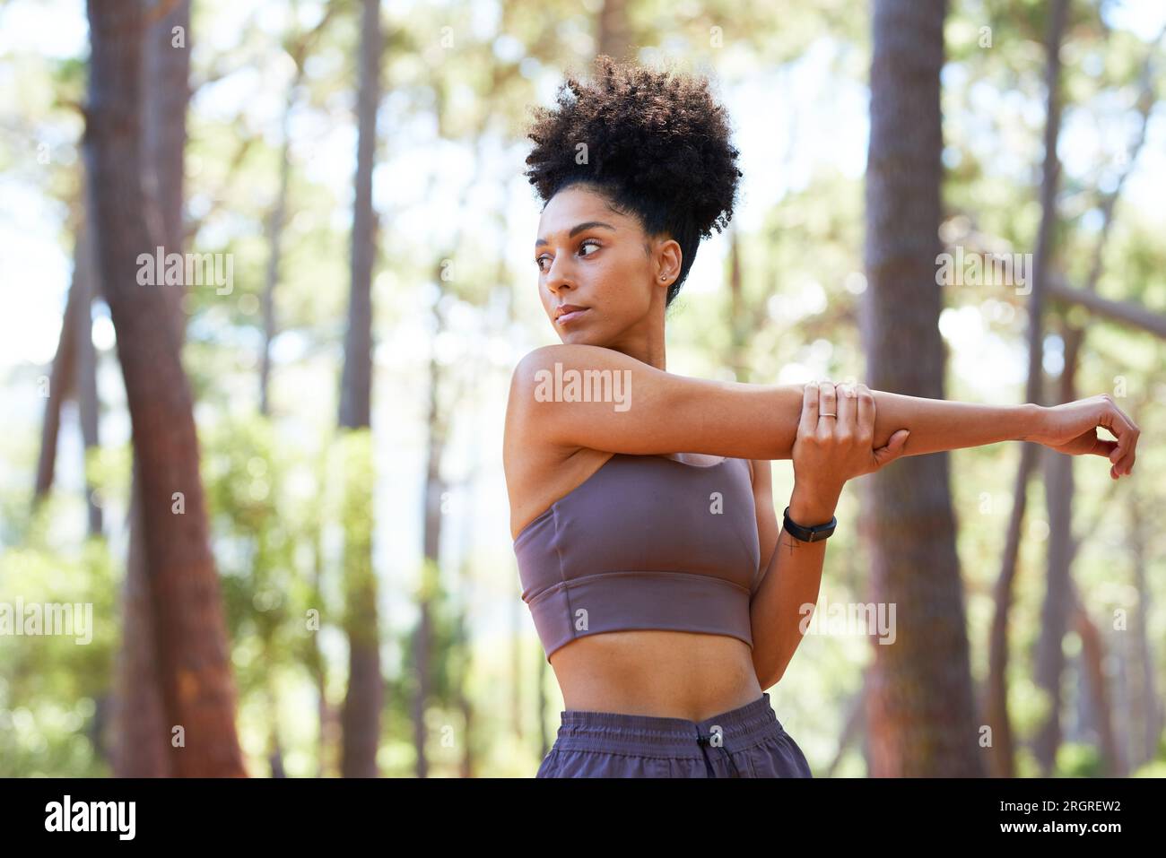 Serious multi-ethnic woman stretches arms before trail run in forest ...