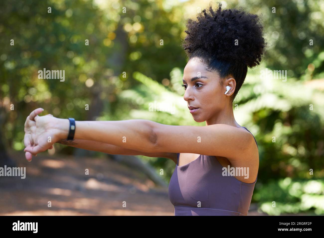 Serious multi-ethnic woman stretches arms before trail run in forest ...