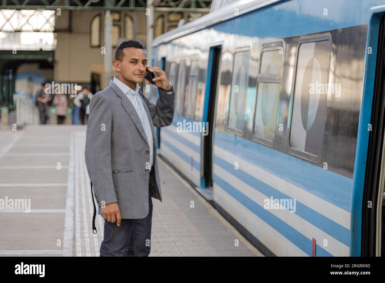 Young latin man talking on a mobile phone on the platform of a train station with copy space. Stock Photo