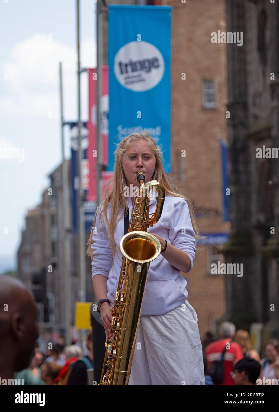 Royal Mile, Scotland, UK. 11 August 2023. Street Performers on High Street finding the windy conditions difficult but hot weather welcome with temperature just over 20 degrees. Crowds arriving later in the day with several other performing pitches around the city centre. Pictured: A female saxophone player attracts people to her colleagues handing out flyers. Credit: Archwhite/alamy live news. Stock Photo
