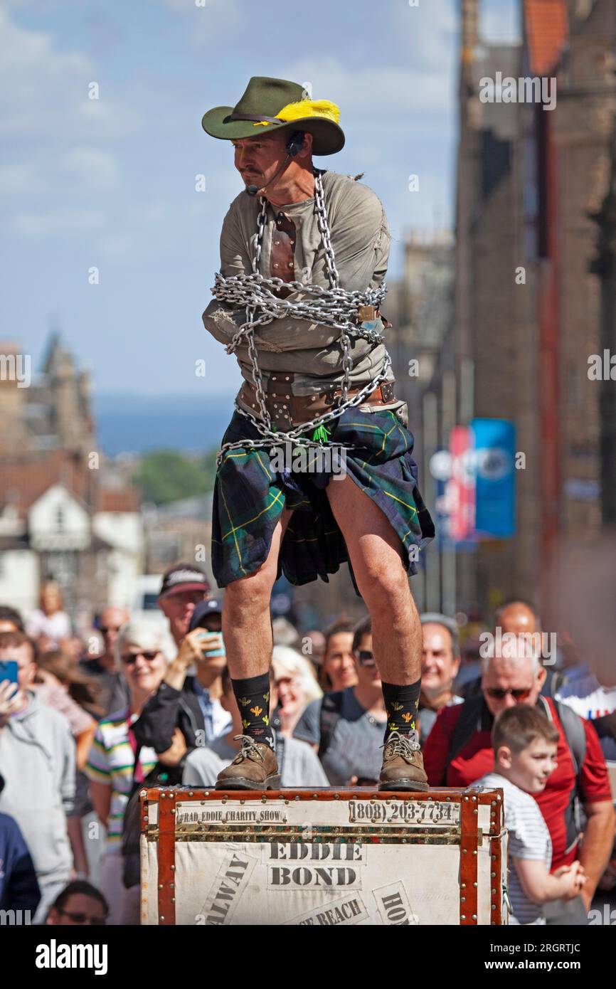 Royal Mile, Scotland, UK. 11 August 2023. Street Performers on High Street finding the windy conditions difficult but hot weather welcome with temperature just over 20 degrees. Crowds arriving later in the day with several other performing pitches around the city centre. Street Performer Eddie Bond all tied up in chains and straight jacket. Credit: Archwhite/alamy live news. Stock Photo