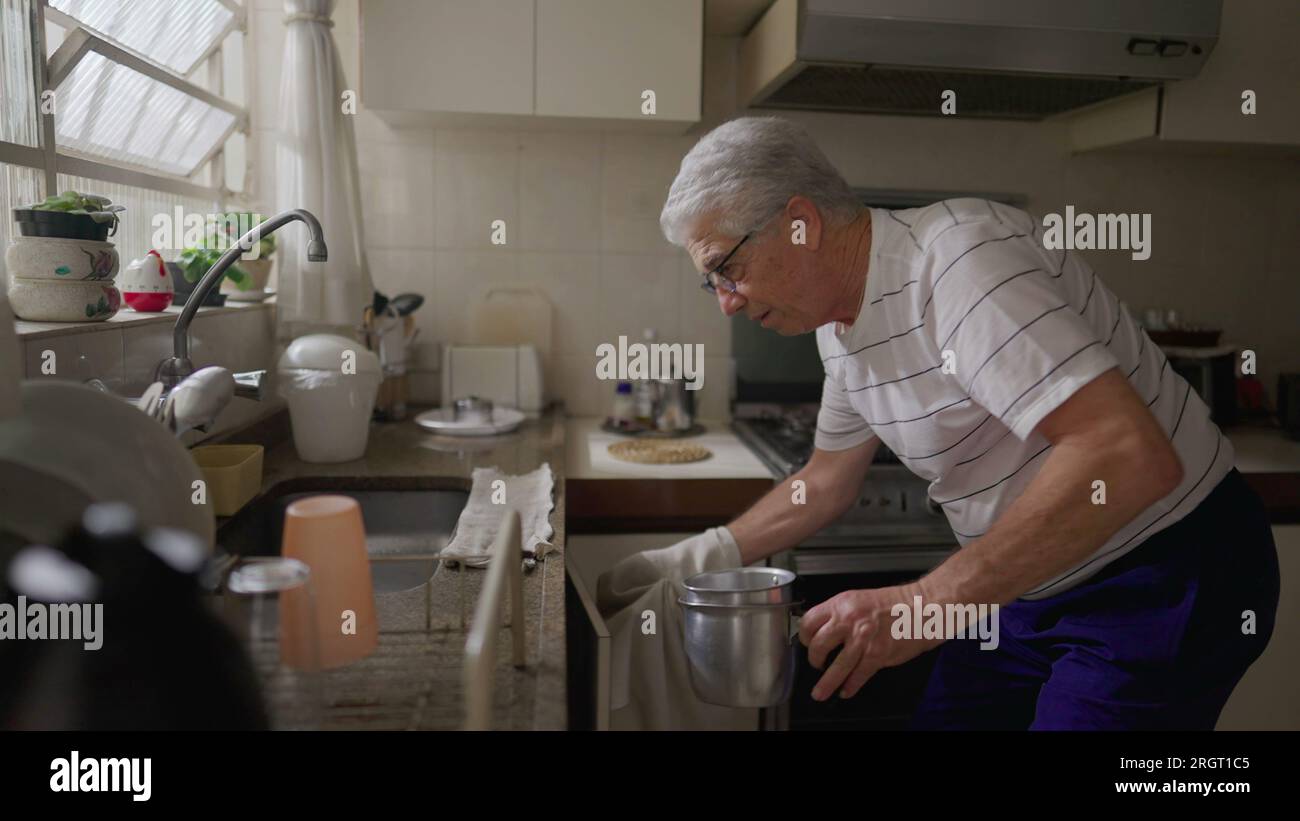 Senior man standing in kitchen sink organizing pots and pans by window