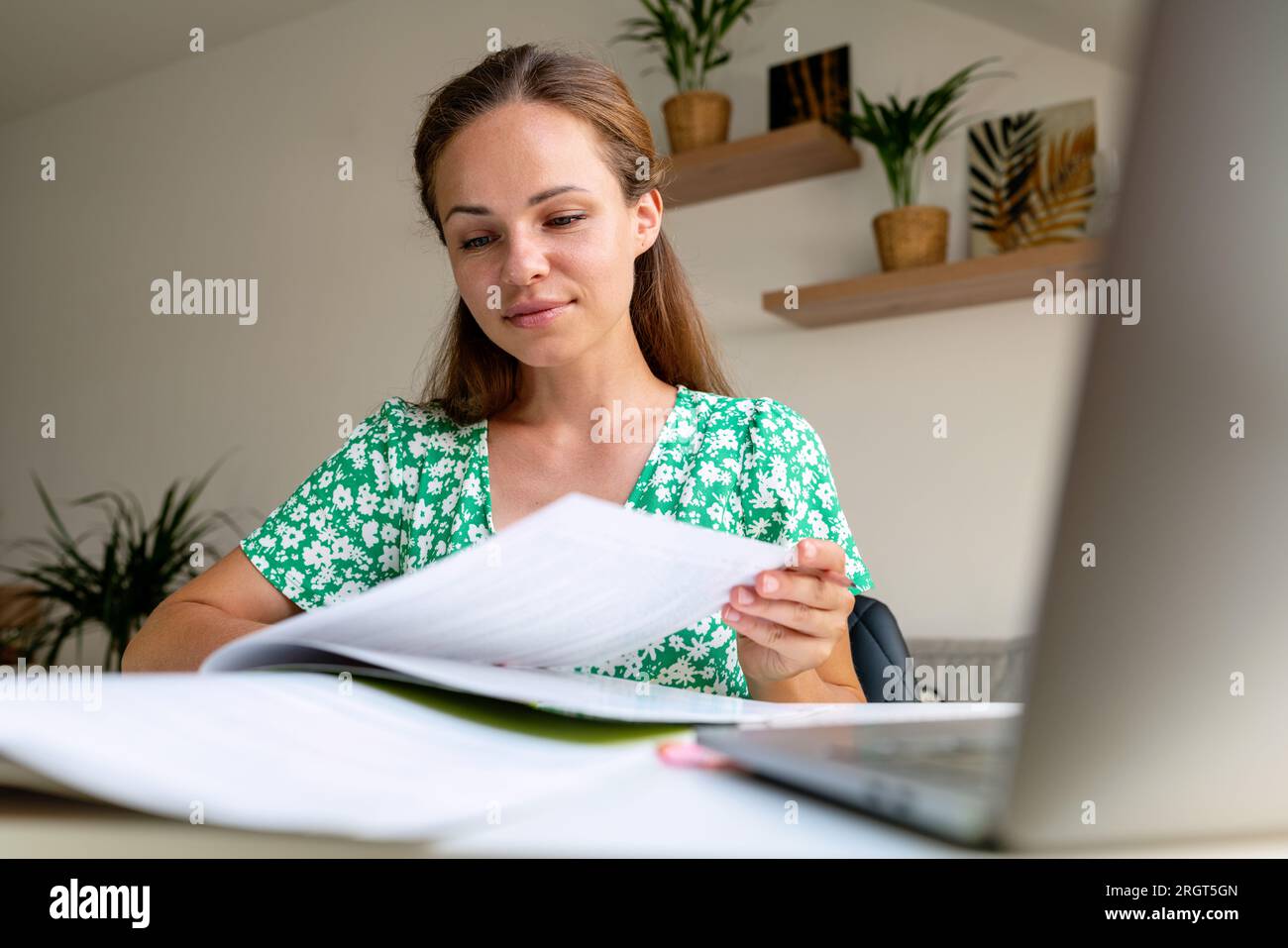 Confident purposeful adult student woman self-studying at home, sitting at the desk and reading student's textbook. Stock Photo