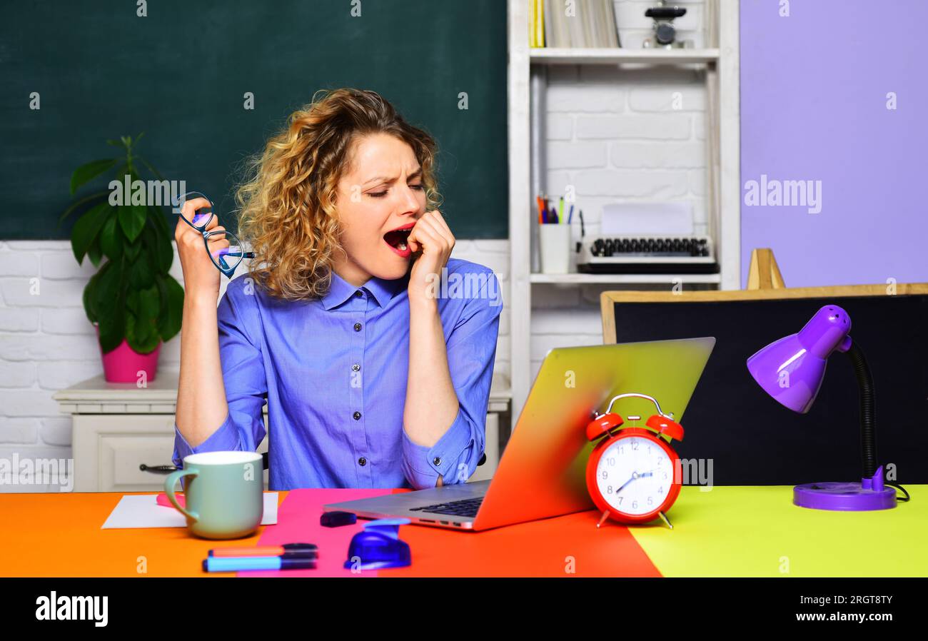 Tired yawning teacher working with laptop in class. Hard work. School professional teacher, female instructor coach at desk. Online test. Fatigued Stock Photo