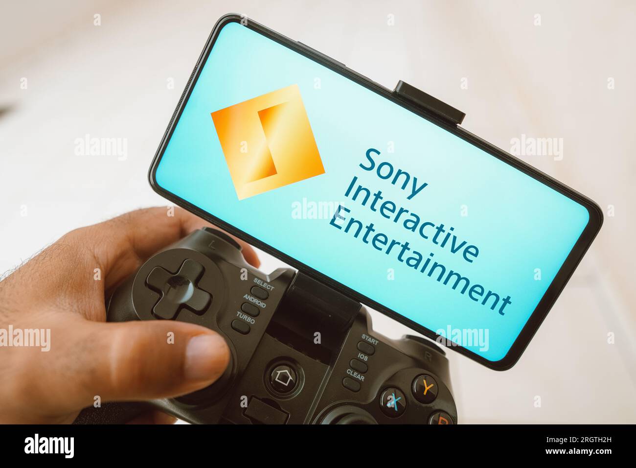 In this photo illustration, a person plays on a joystick and the Sony Interactive Entertainment logo displayed on a smartphone screen. Stock Photo