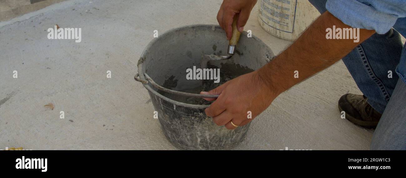 Image of a bricklayer's hands mixing cement and glue in a bucket