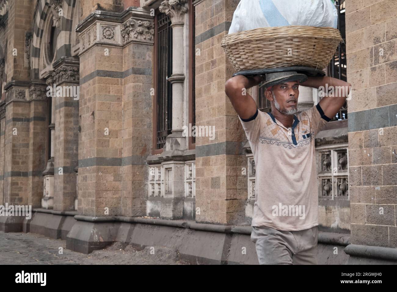 A porter with a basket of fish on his head, outside Chhatrapati Shivaji Maharaj Terminus (CMST), in Mumbai, India, to forward the fish by local train Stock Photo