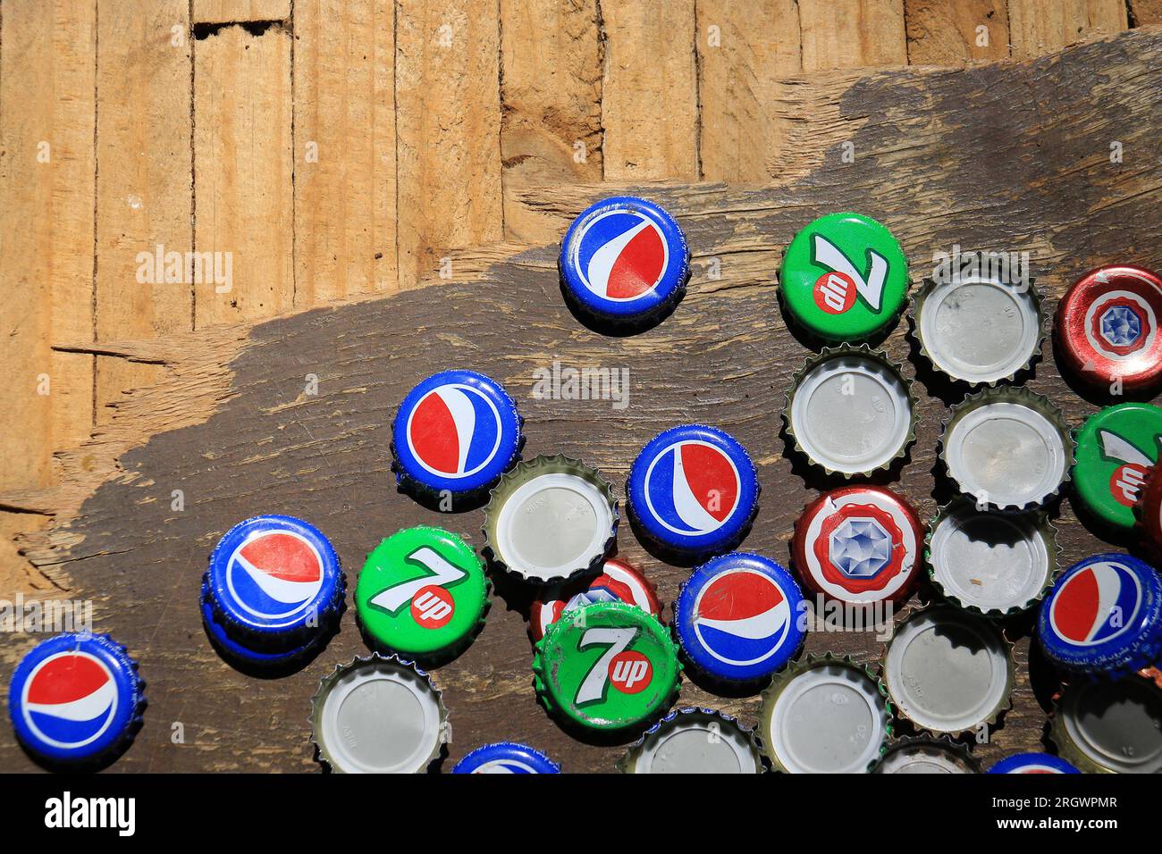 Zgharta, Lebanon - May 28, 2022: Discarded caps of Pepsi Cola, 7Up, and Almaza beer on a wooden table. Stock Photo