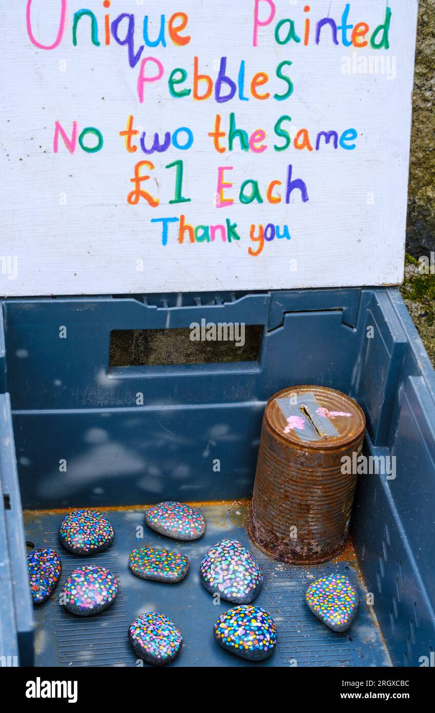 Decorative sign on box of painted stones for sale with old tin can honesty box. Stock Photo