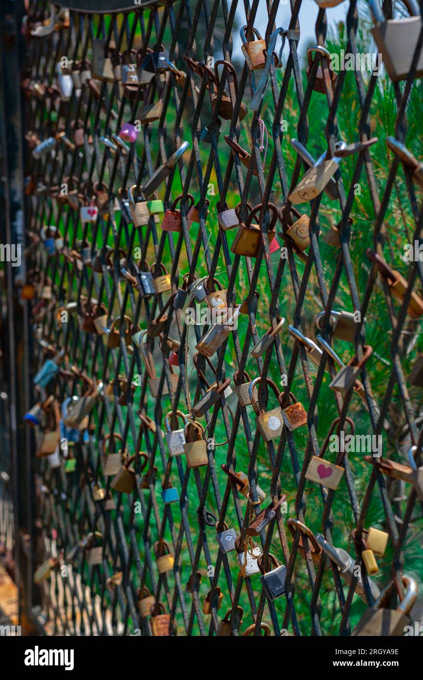 A mesh fence on the seashore with padlocks symbolizing love. Love locks are hung on the fence in large numbers on the sea promenade. Sea on background Stock Photo