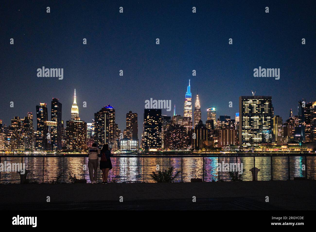Cityscape connection: A couple enjoys the view from Hunter's Point, Long Island City, as Manhattan's skyline illuminates the night over East River Stock Photo