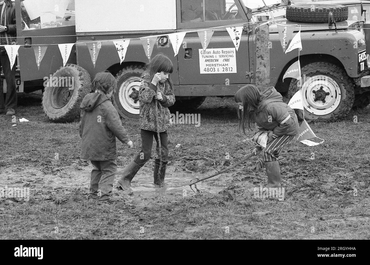 Three young children play in a muddy puddle during an autocross event at Smallfield in Surrey, England on March 6, 1977. Stock Photo