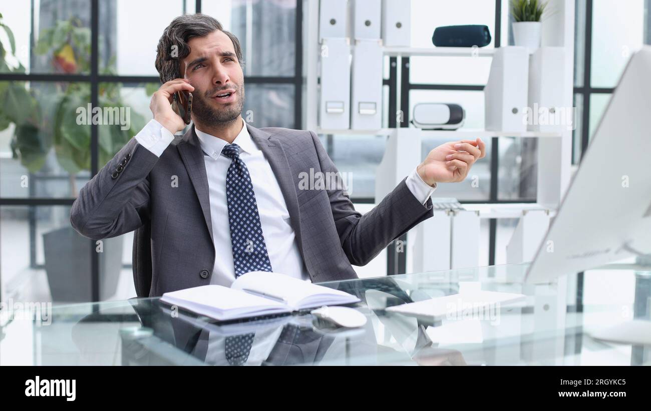 young web developer talking on phone while working with laptop in office Stock Photo