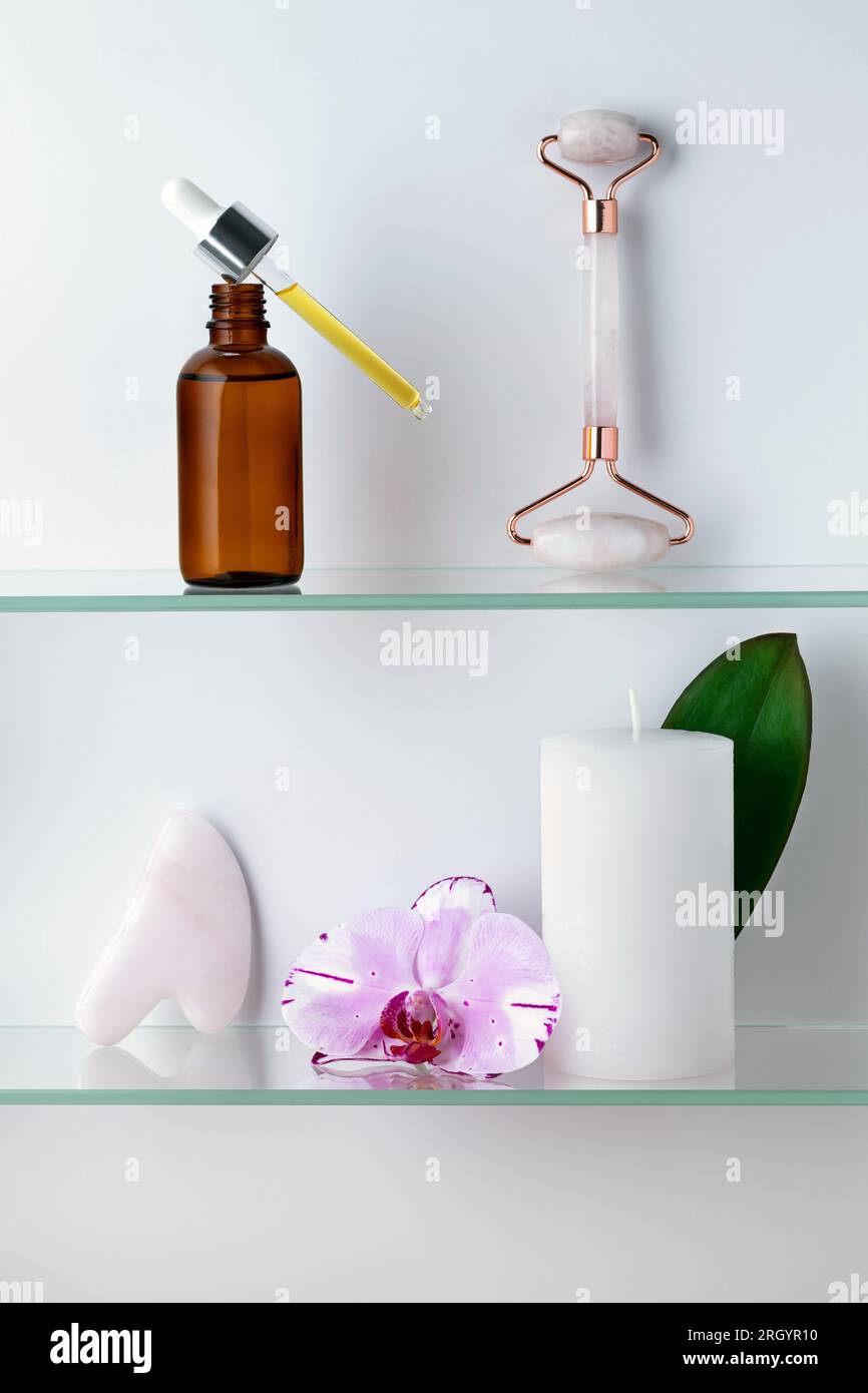 Glass serum bottle with pipette, scented white candle in the bathroom. Gua Sha massage tool. Natural oil. Orchid flower. Spa treatments and beauty. An Stock Photo