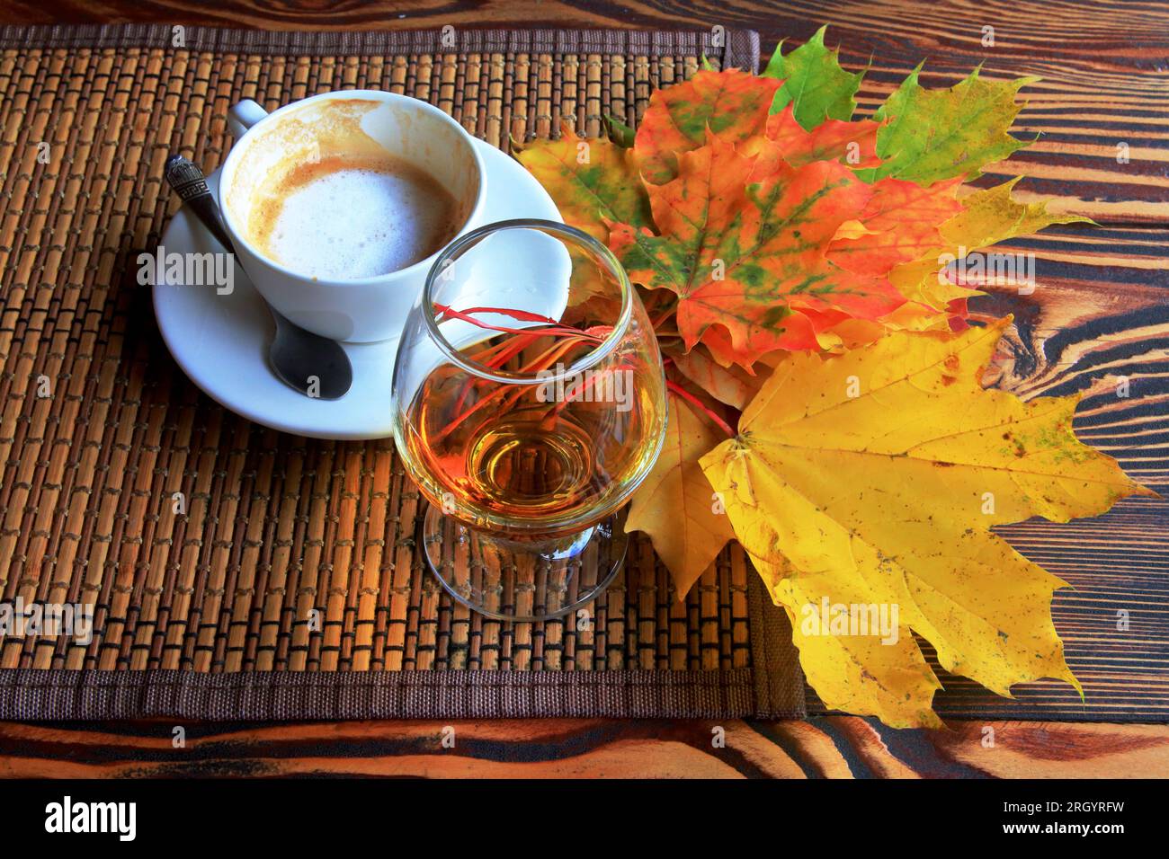 the photo shows an autumn still life with a cup of coffee, a glass of brandy and bright leaves. Stock Photo