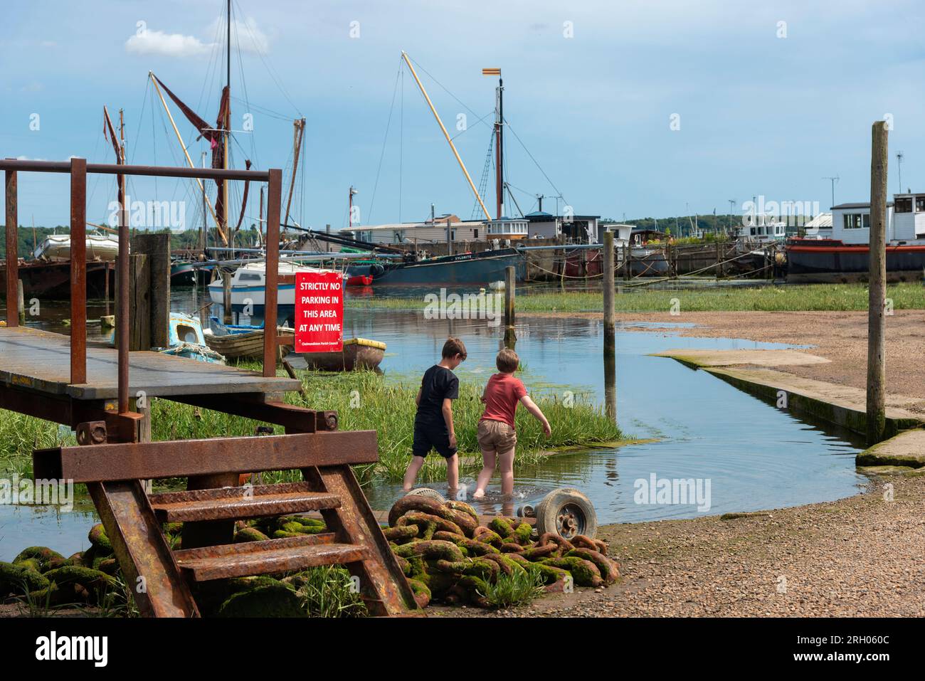 Two boys in summer 2023 playing in the water on an incoming tide in the picturesque waterside village of Pin Mill, Suffolk, East Anglia, England Stock Photo