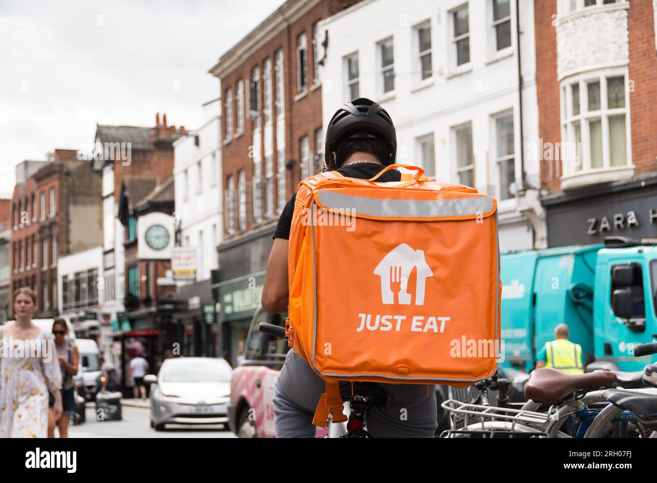 A Just Eat delivery driver sitting upon his bicycle with a large orange Just Eat insulated backpack container resting on his back. Richmond, Surrey Stock Photo