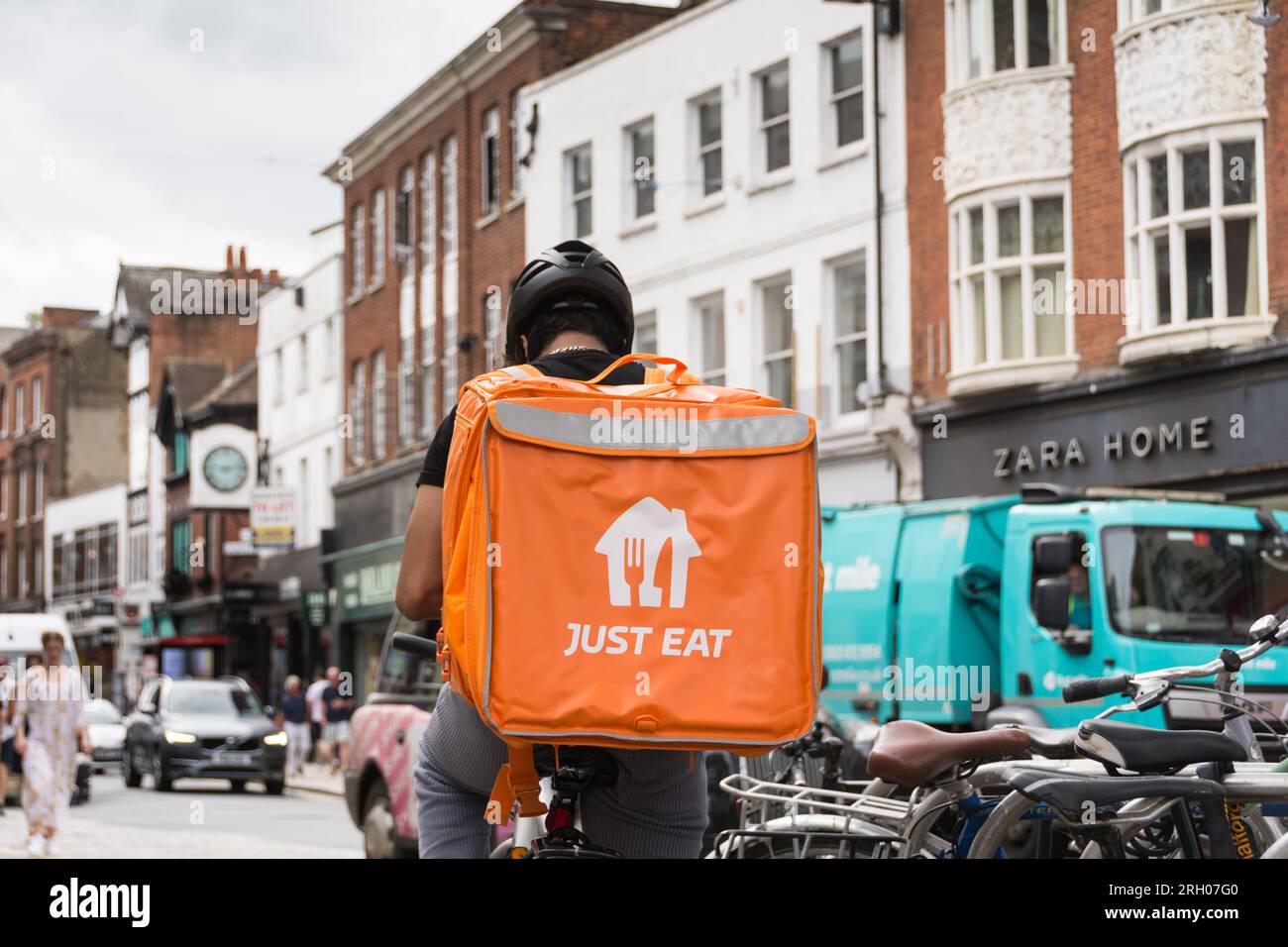 A Just Eat delivery driver sitting upon his bicycle with a large orange Just Eat insulated backpack container resting on his back. Richmond, Surrey Stock Photo