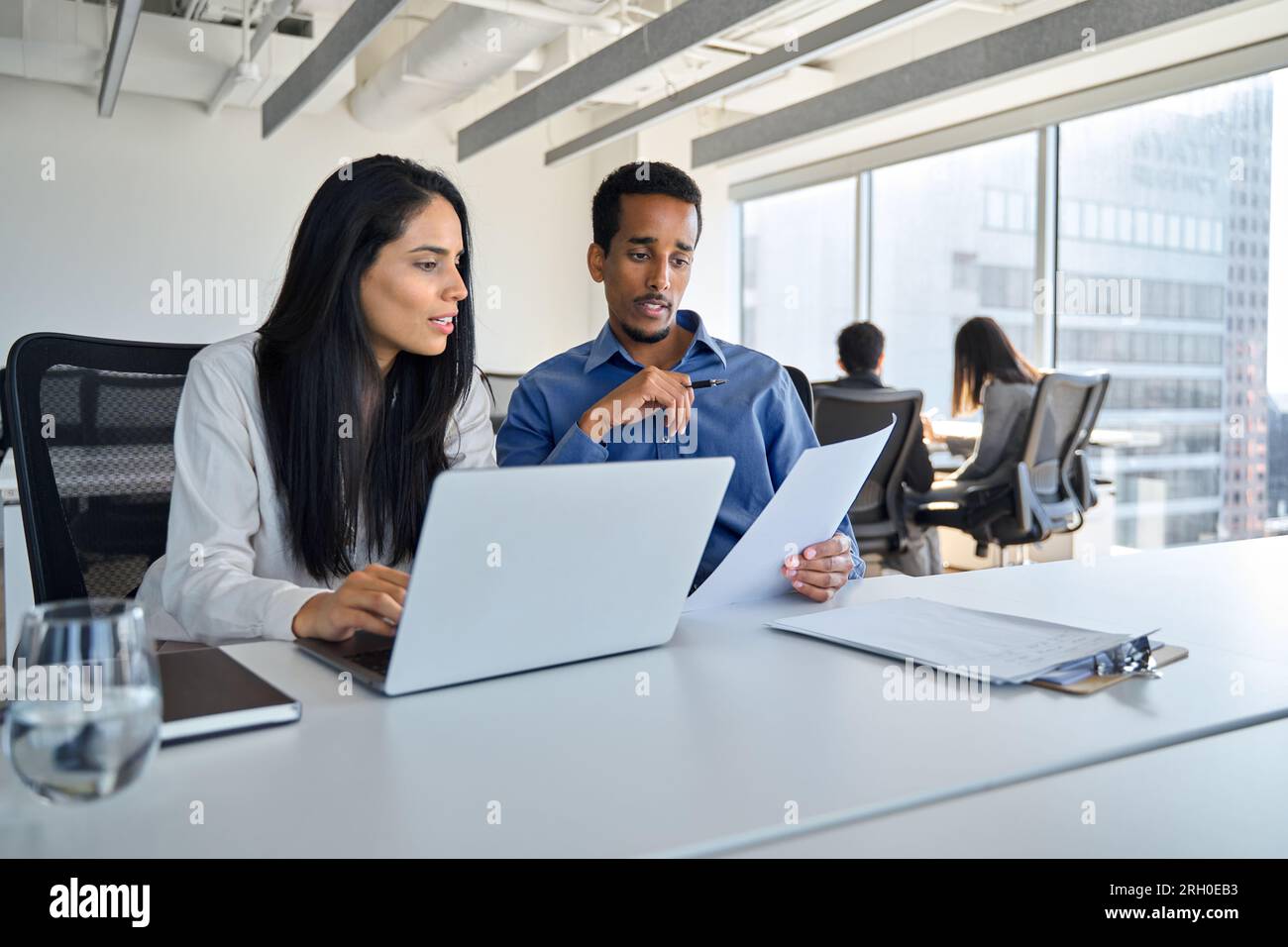 Diverse employees using laptop discussing business documents working in office. Stock Photo