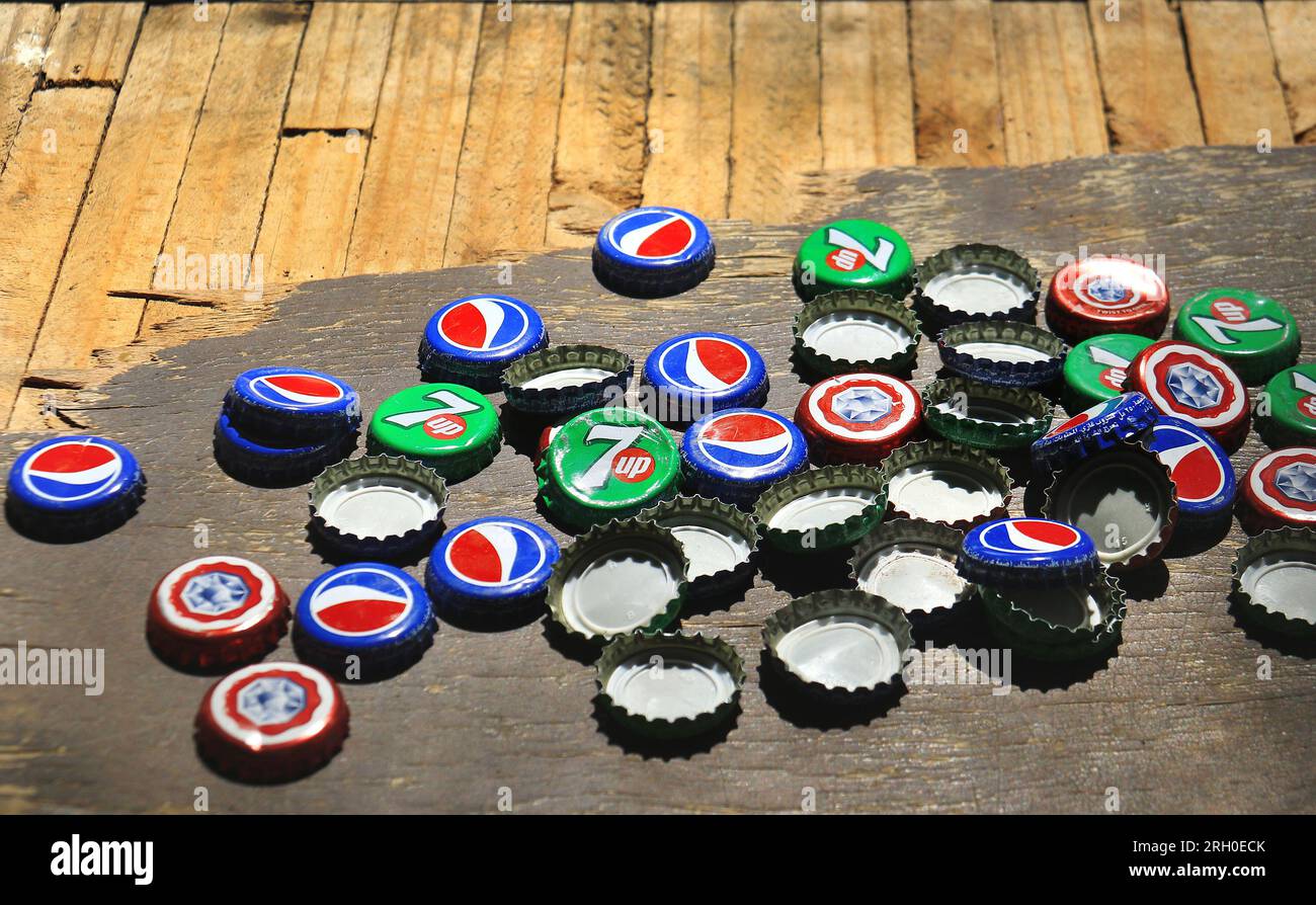 Zgharta, Lebanon - May 28, 2022: Discarded caps of Pepsi Cola, 7Up, and Almaza beer on a wooden table. Stock Photo