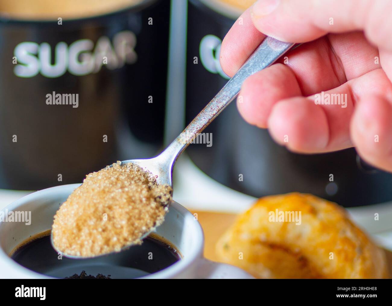 Freshly poured espresso,hot and ready to drink at breakfast,a silver spoon about to mix in brown sugar to sweeten,on a wood board, a bread roll,sugar Stock Photo