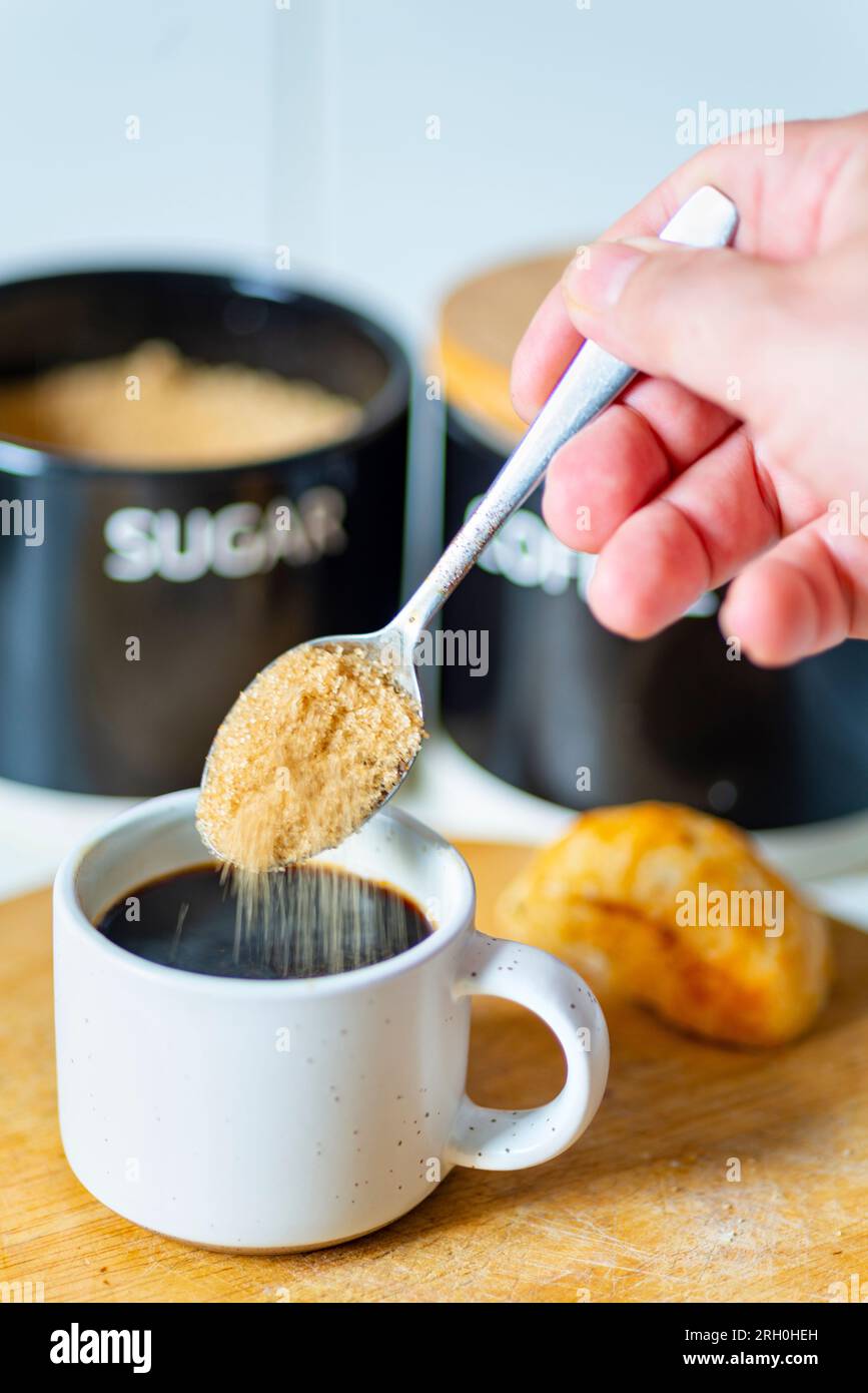 Grains of brown sugar drop from a spoon,about to be srirred into a freshly brewed black espresso,ready to drink,hot and sweet at breakfast time,a brea Stock Photo