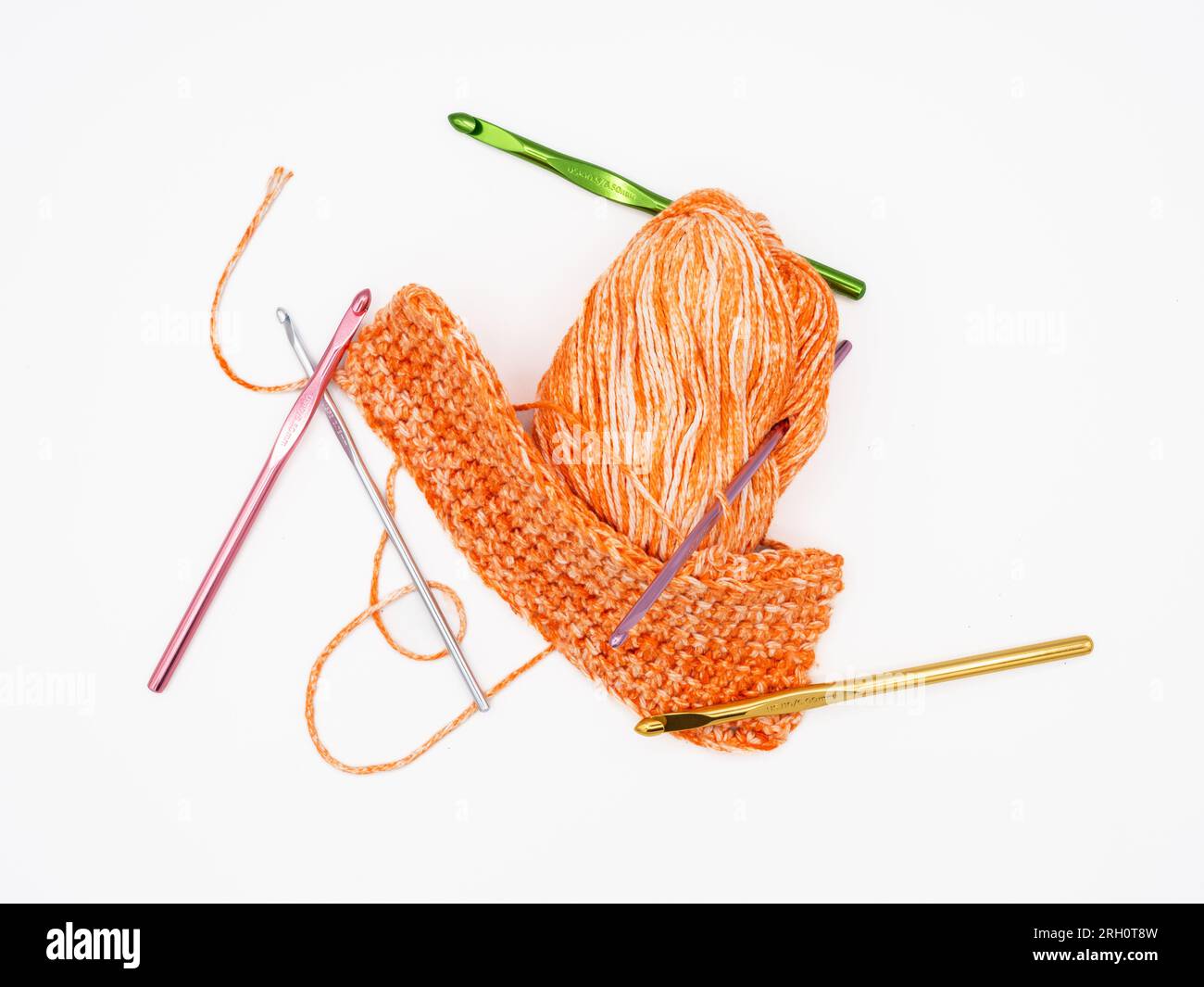 On a white background, there's pumpkin-colored yarn alongside multiple crochet hooks in assorted colors, all isolated. Stock Photo