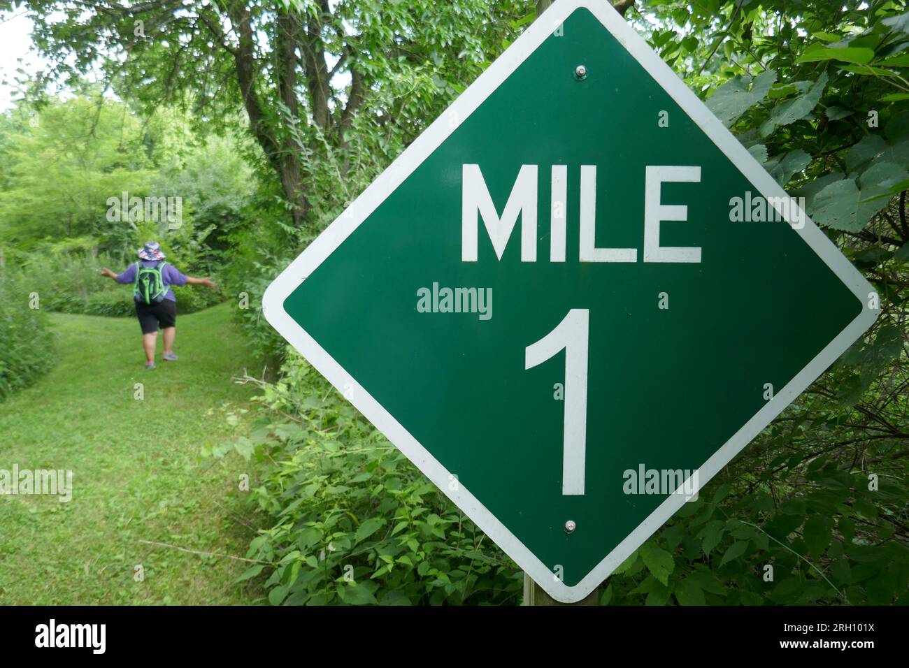 Mile 1 marker sign on hiking trail in nature park with blurred woman in background acting like she is lost Stock Photo