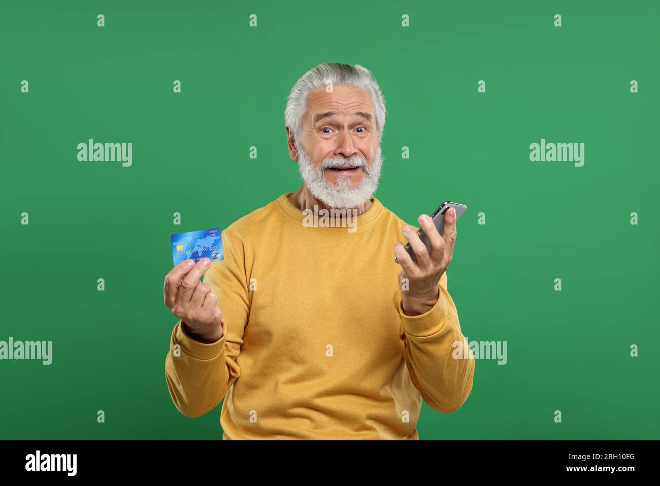 Stressful senior man with credit card and smartphone on green background. Be careful - fraud Stock Photo