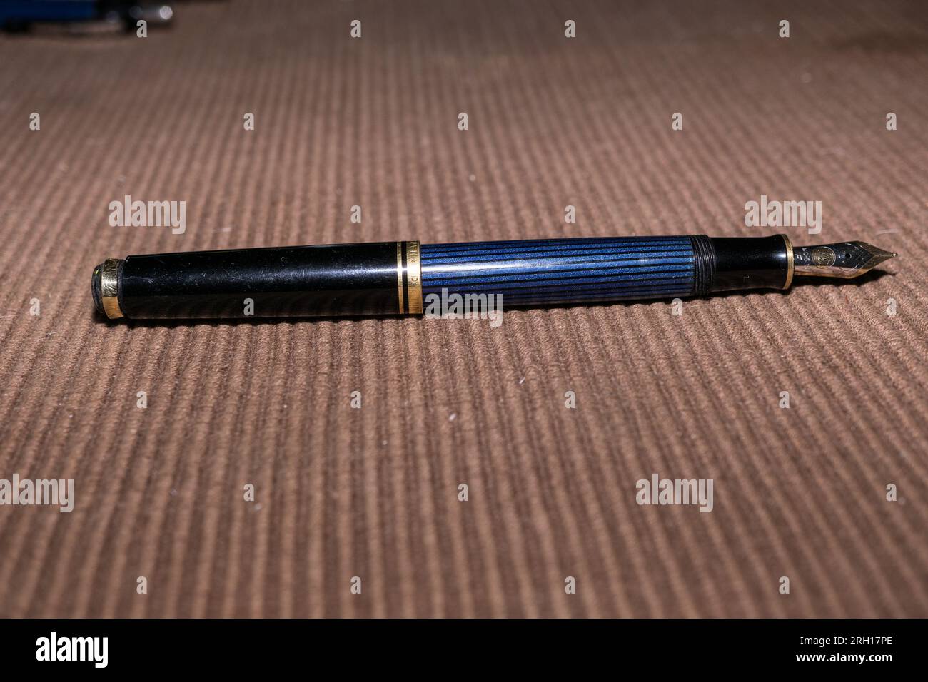 A Pelikan Souveran M600 Fountain Pen lies on a brown placemat.  This is a medium sized Pelikan with a 14 carat gold nib with an iridium tip. Stock Photo