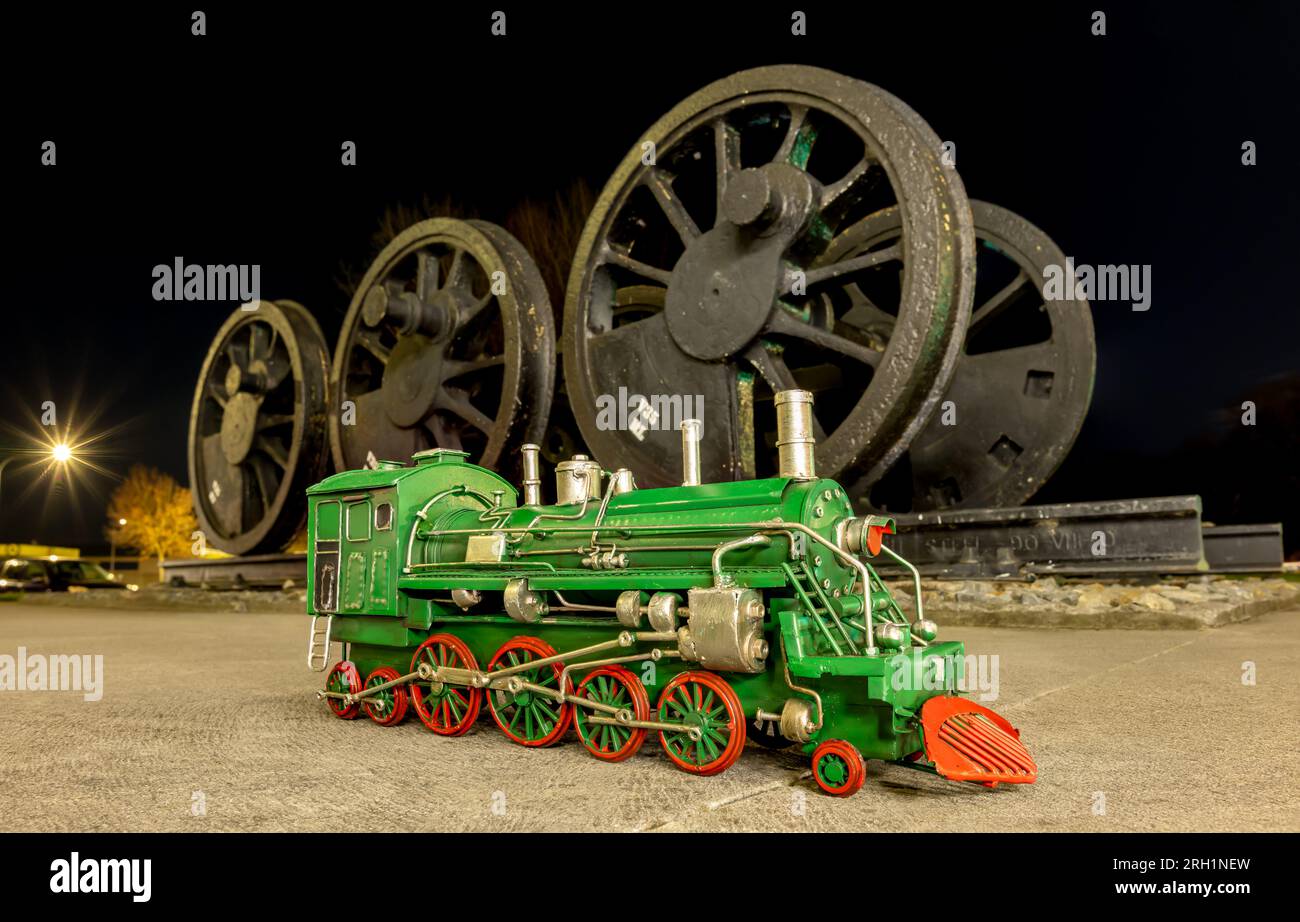 Green steam locomotive model with red wheels in front of a set of old steam locomotive wheels. Stock Photo