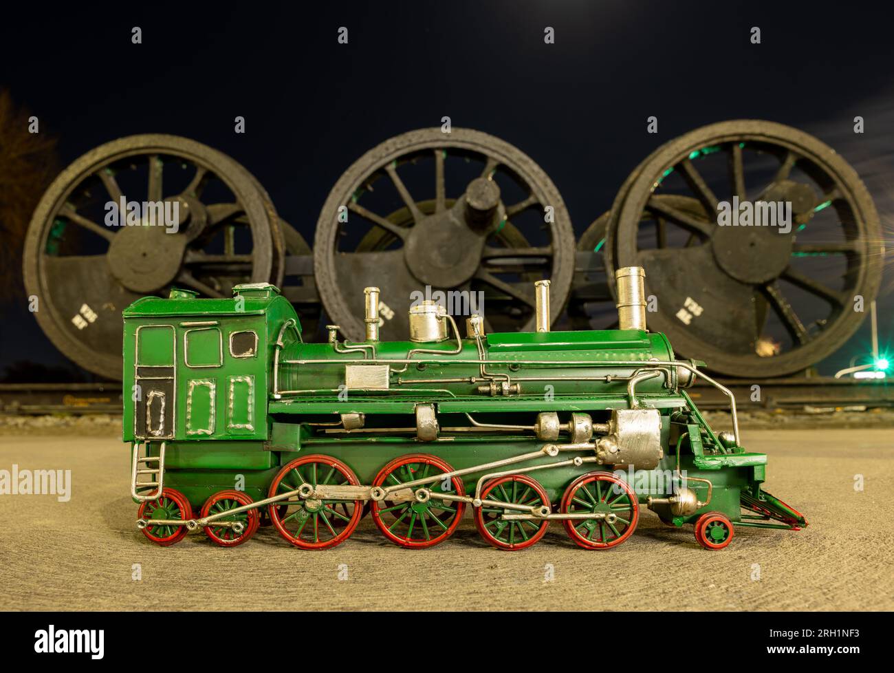 Green steam locomotive model with red wheels in front of a set of old steam locomotive wheels. Stock Photo
