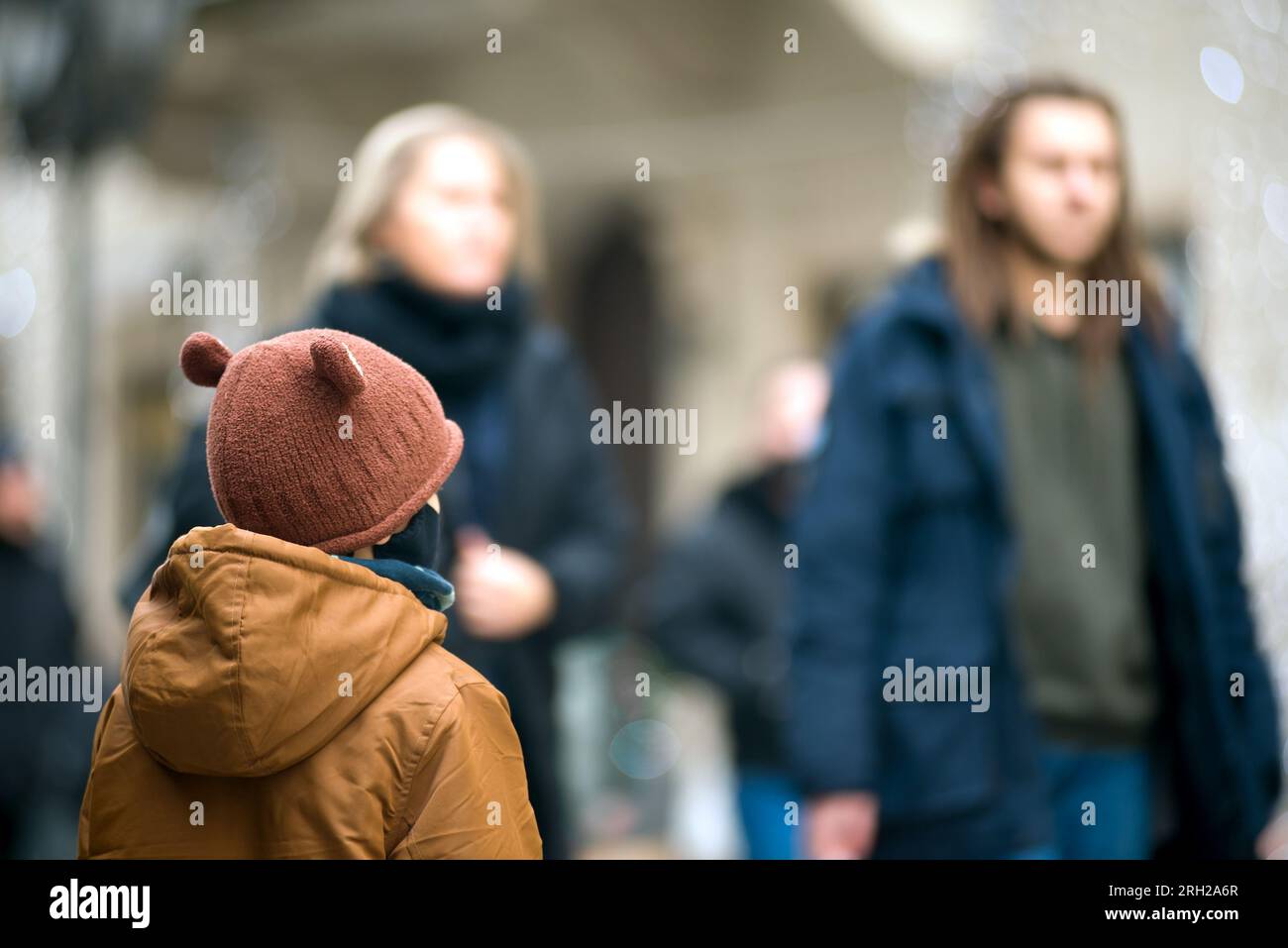 Child on the street watching defocused people passing by Stock Photo