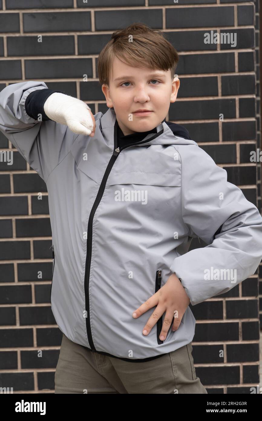 A tenyearold boy in a gray jacket with a cast on his arm Stock Photo