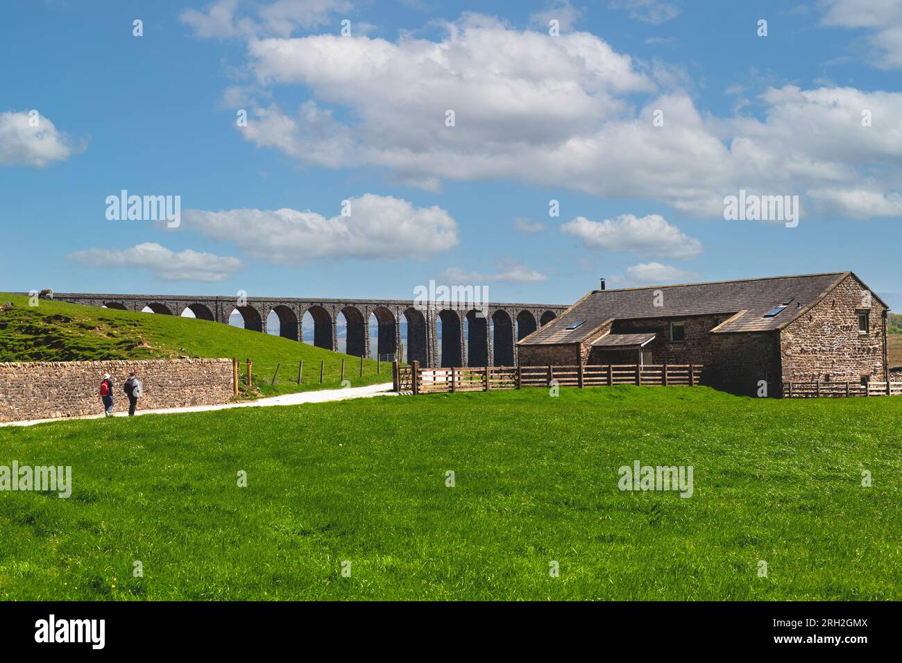 Ribblehead Viaduct in the North Yorkshire Dales. Two hackers walking near traditional stone farm buildings. Stock Photo