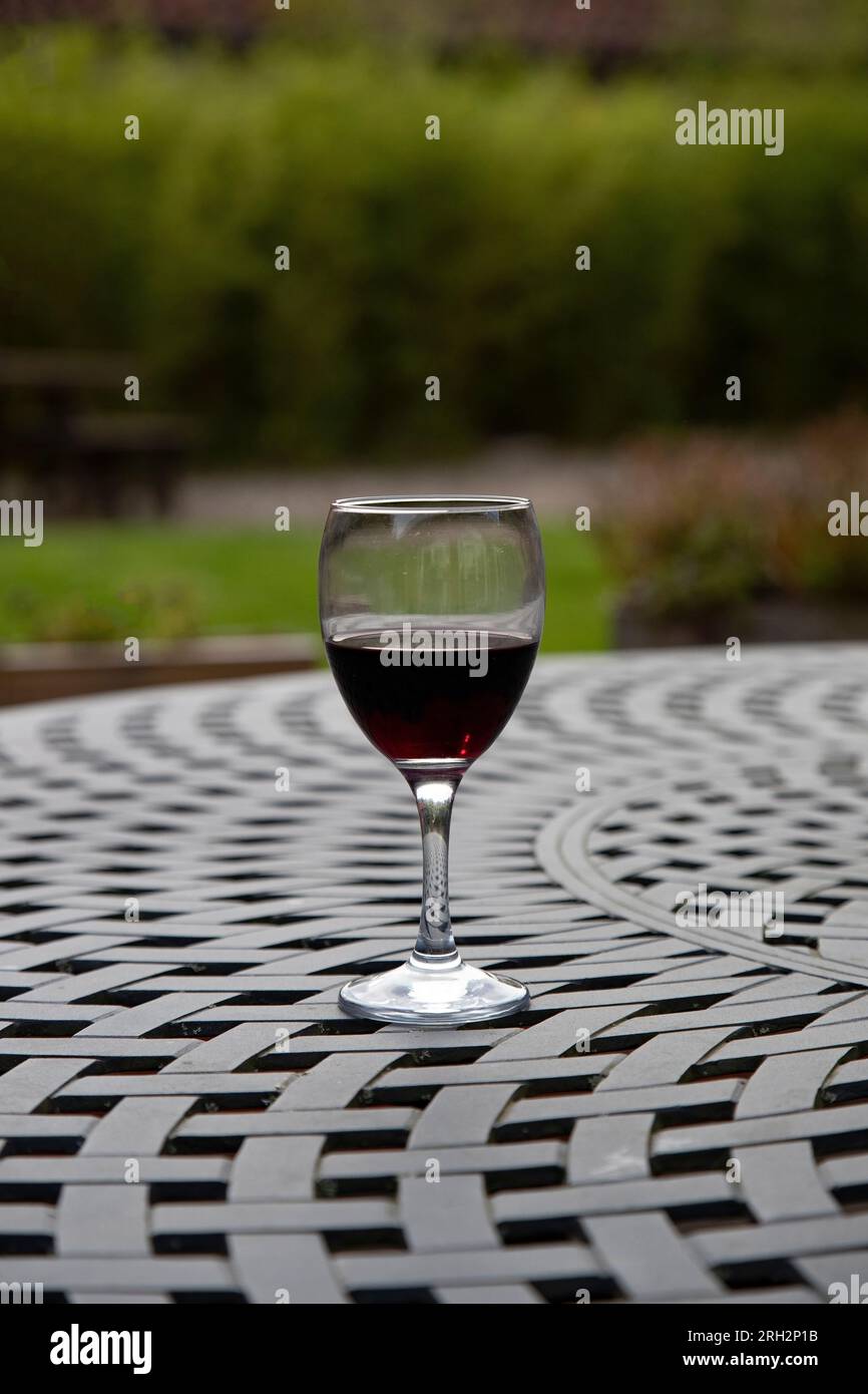 A single glass of red wine on an outdoor table during summer in East Yorkshire, U.K. Stock Photo