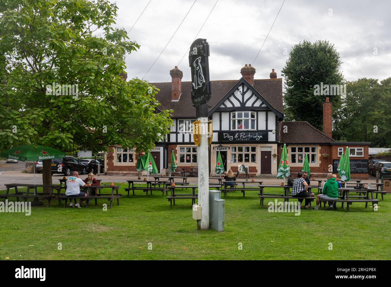 The Dog & Partridge pub in Yateley, Hampshire, England, UK, with people sitting at outside tables having drinks on the grass Stock Photo