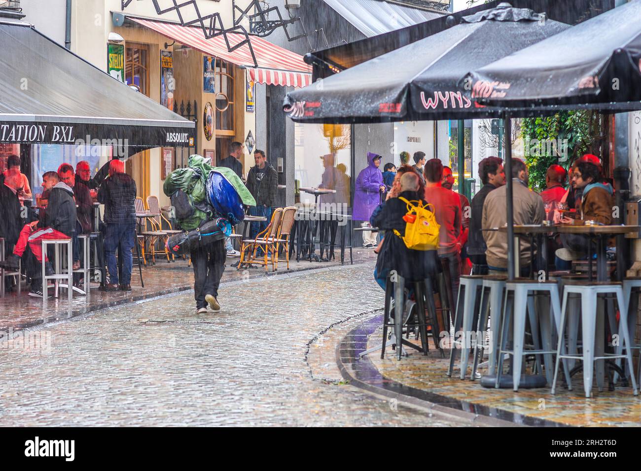 Traveler with rucksack and baggage walking along city center street in pouring rain - Brussels, Belgium. Stock Photo