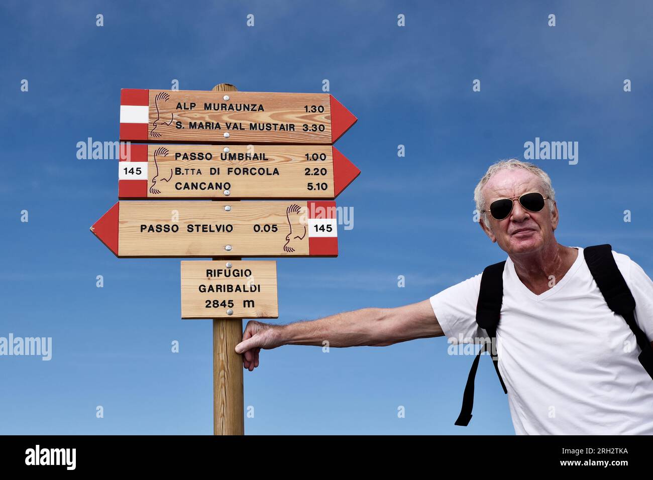 A sporty, older man in sunglasses and a daypack leans on top of an ...
