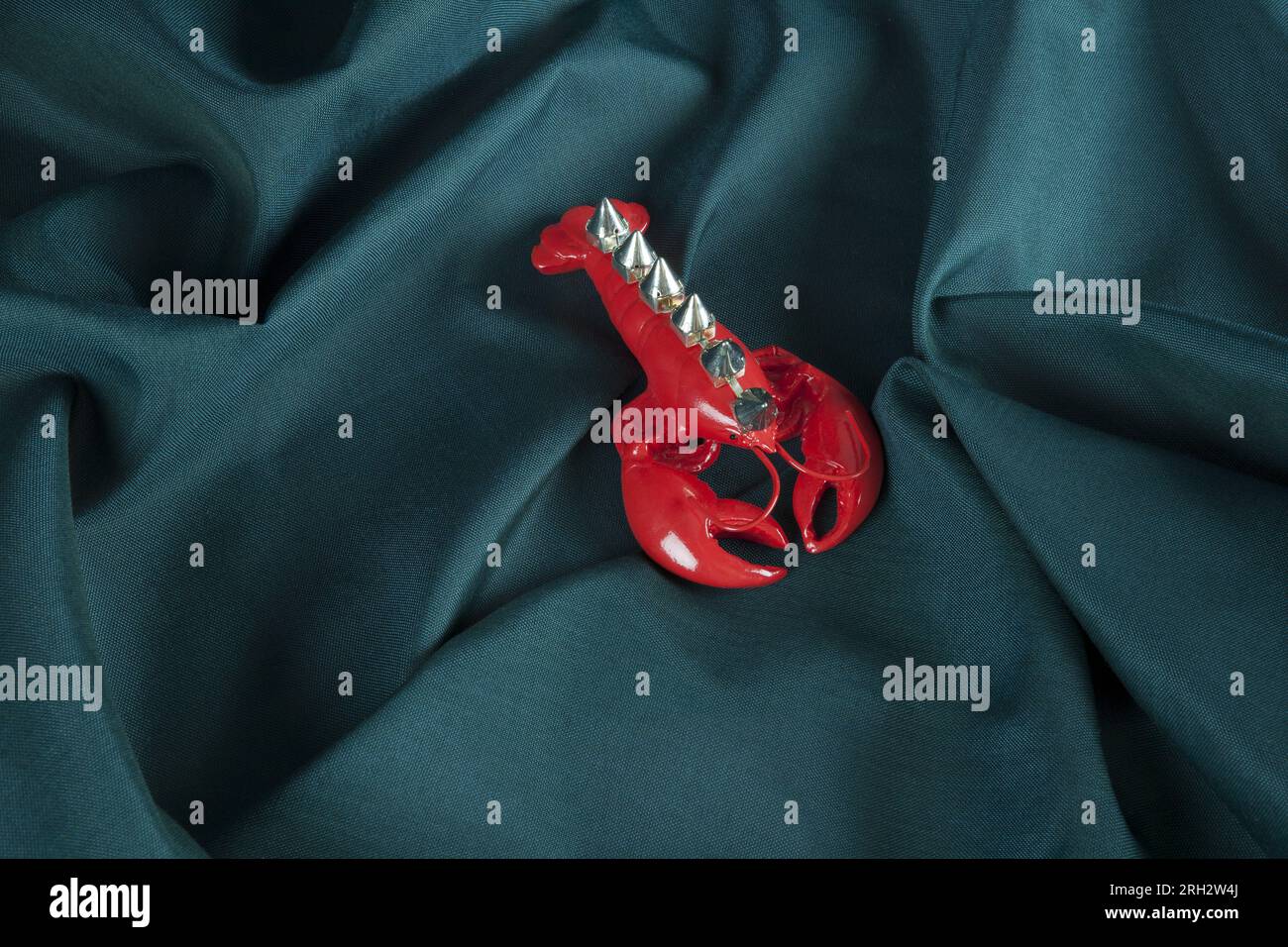 a punk style lobster wearing riveted spikes like a mohican on a green wavy fabric background. Minimal color still life photography. Stock Photo