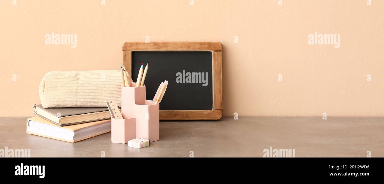 Stylish cup with stationery, books and chalkboard on table against beige background. Banner for design Stock Photo