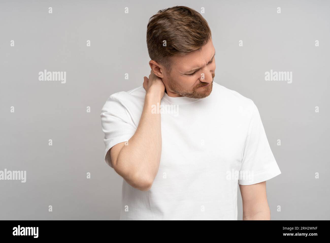 Unhealthy middle age man suffers from pain in neck after sleep standing on grey studio copy space Stock Photo