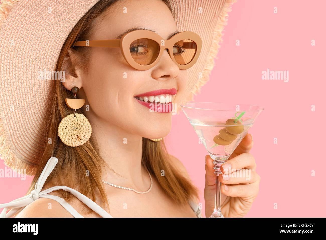 Beautiful young woman in wicker hat with glass of martini on pink background Stock Photo