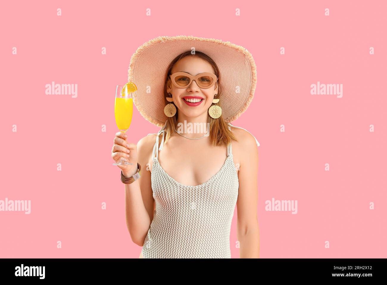 Beautiful young woman in wicker hat with glass of tasty citrus cocktail on pink background Stock Photo