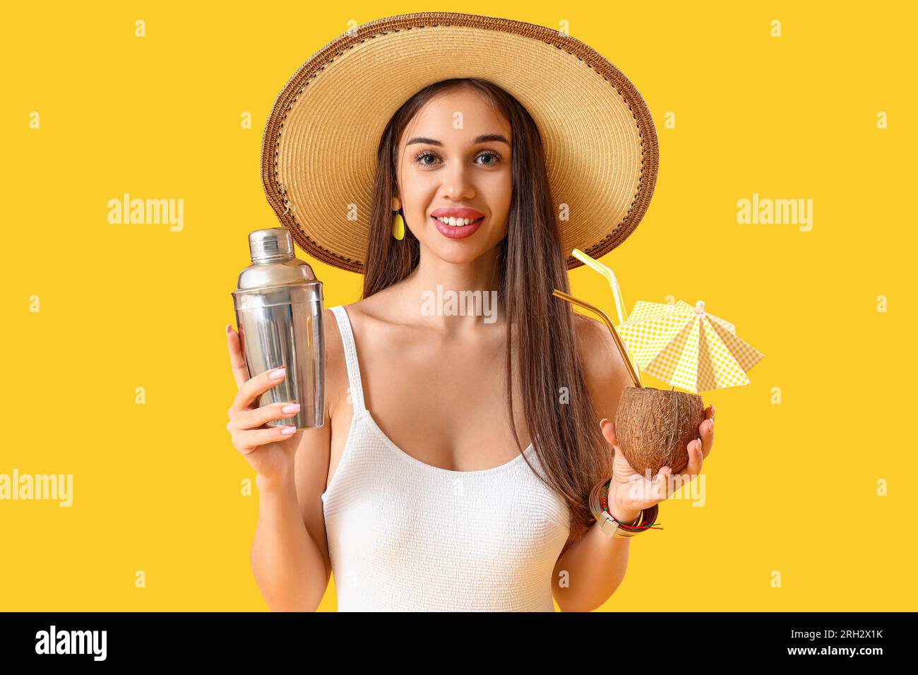Beautiful young woman with shaker and tasty cocktail in coconut on yellow background Stock Photo
