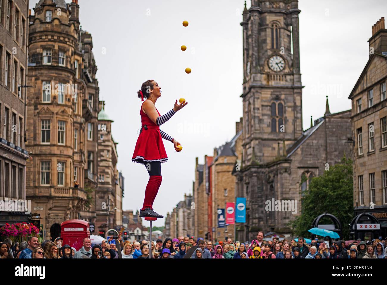 Royal Mile, Edinburgh, Scotland, UK. 13 August 2023. Edinburgh Festival Fringe performers suffered heavy downpours during their shows on the High Street on the second Sunday of the arts festival, the brollies went up, waterproofs on and the audiences in the most part stuck around. Pictured:StreetPerformer Kate the Great demonstrates her balance and juggling skills to a very wet audience on the Royal Mile. Credit: Archwhite/alamy live news. Stock Photo